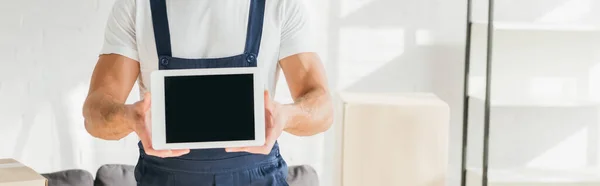 Vista recortada de mover en uniforme celebración tableta digital con pantalla en blanco cerca de cajas en el apartamento, pancarta - foto de stock