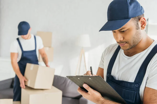 Trabalhador indiano escrevendo na área de transferência perto colega de trabalho em fundo turvo — Stock Photo