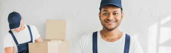 Fröhlicher indischer Arbeiter, der auf verschwommenem Hintergrund in die Kamera neben einem Kollegen blickt, Banner — Stockfoto