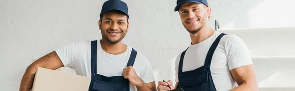 Movimentadores multiculturais alegres sorrindo enquanto olha para a câmera no apartamento, banner — Fotografia de Stock