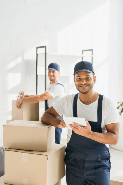 Lächelnder indischer Mover hält digitales Tablet neben Mitarbeiter auf verschwommenem Hintergrund — Stockfoto