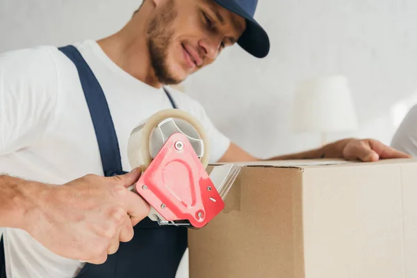 Happy mover packing box with scotch tape in apartment — Stock Photo