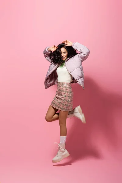 Brunette young woman in stylish winter outfit jumping on pink background — Stock Photo