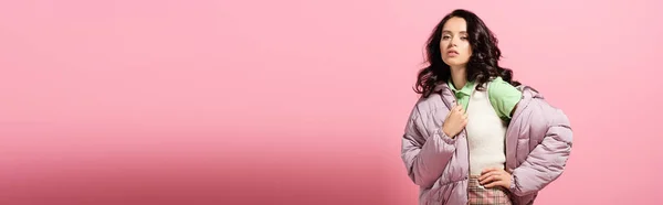Brunette young woman in puffer jacket posing on pink background, banner — Stock Photo