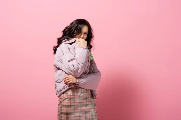 Brunette young woman in puffer jacket posing on pink background — Stock Photo