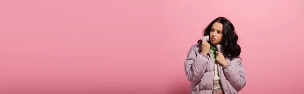 Brunette young woman in puffer jacket posing on pink background, banner — Stock Photo