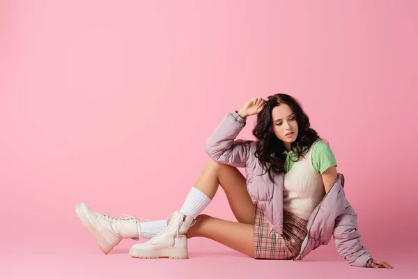 Side view of brunette young woman in stylish winter outfit posing on floor on pink background — Stock Photo