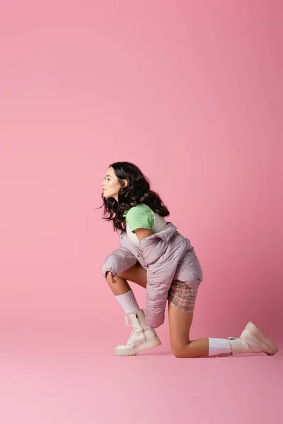 Side view of brunette young woman in stylish winter outfit posing on floor on pink background — Stock Photo