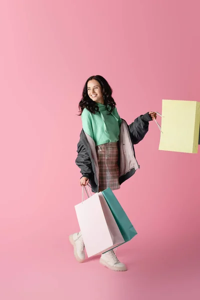 Happy brunette young woman in casual winter outfit with shopping bags on pink background — Stock Photo