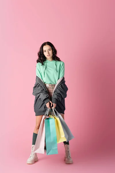 Morena mujer joven en traje casual de invierno con bolsas de compras sobre fondo rosa — Stock Photo