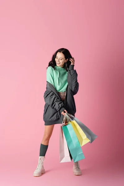 Sonriente morena joven en traje casual de invierno con bolsas de compras sobre fondo rosa - foto de stock