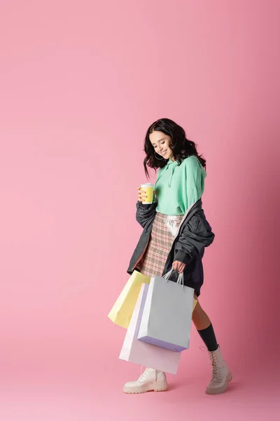 Sorrindo morena jovem em roupa de inverno casual com sacos de compras e café para ir em fundo rosa — Fotografia de Stock