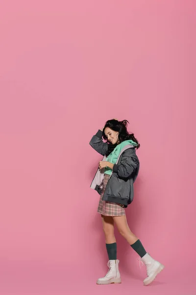 Улыбающаяся брюнетка молодая женщина в повседневной зимней одежде позирует на розовом фоне — стоковое фото