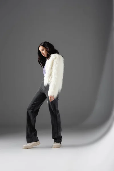 Brunette young woman in stylish white faux fur jacket posing on grey background — Stock Photo