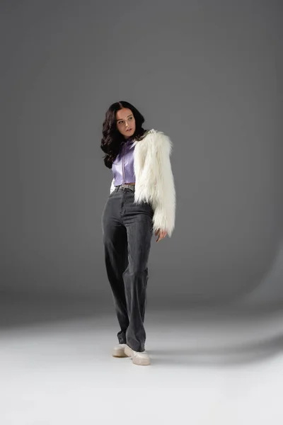 Morena mujer joven en elegante chaqueta de piel sintética blanca posando sobre fondo gris - foto de stock