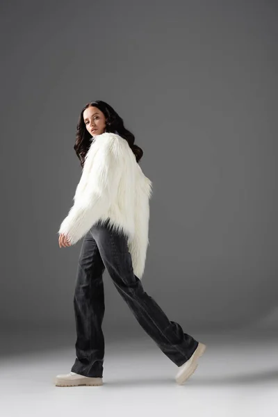 Brunette young woman in stylish white faux fur jacket posing on grey background — Stock Photo