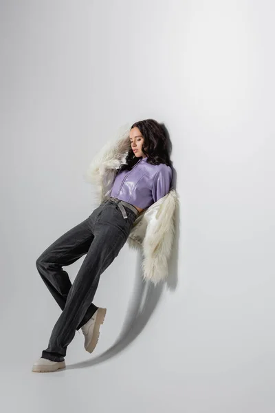 Brunette young woman in stylish white faux fur jacket posing on grey background — Stock Photo