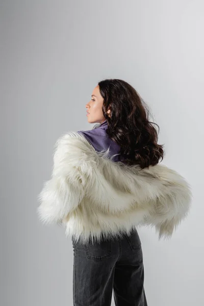 Brunette young woman in stylish white faux fur jacket posing on grey background — Stock Photo