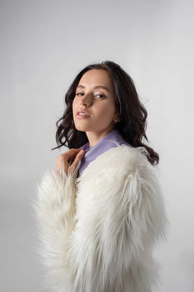 Brunette young woman in stylish white faux fur jacket posing on grey background — Stock Photo