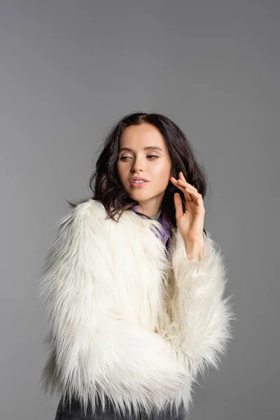 Элегантная брюнетка молодая женщина в стильном белом искусственном меховом пиджаке позирует на сером фоне — стоковое фото