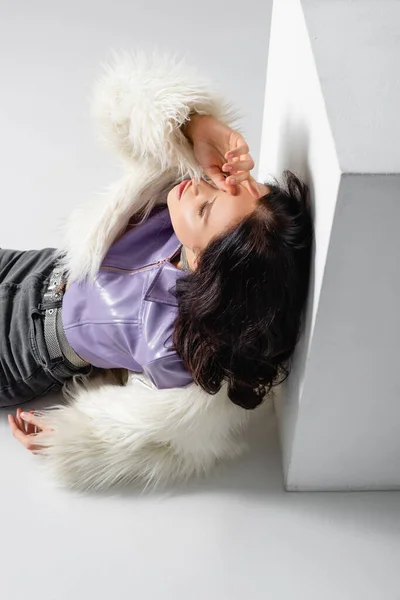 Elegant brunette young woman in stylish faux fur jacket posing near cube on white background — Stock Photo