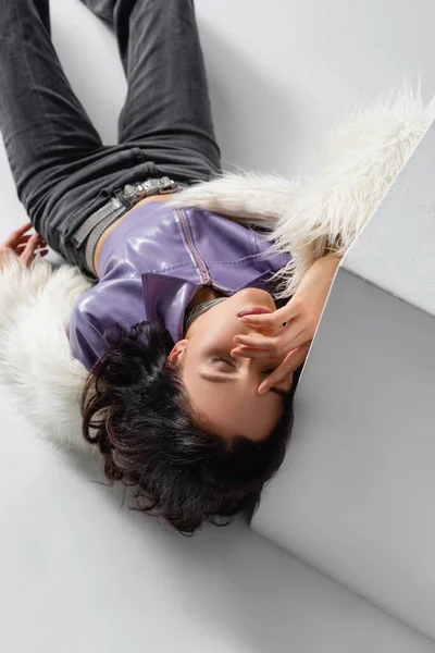 Elegante bruna giovane donna in elegante giacca di pelliccia sintetica posa vicino cubo su sfondo bianco — Foto stock