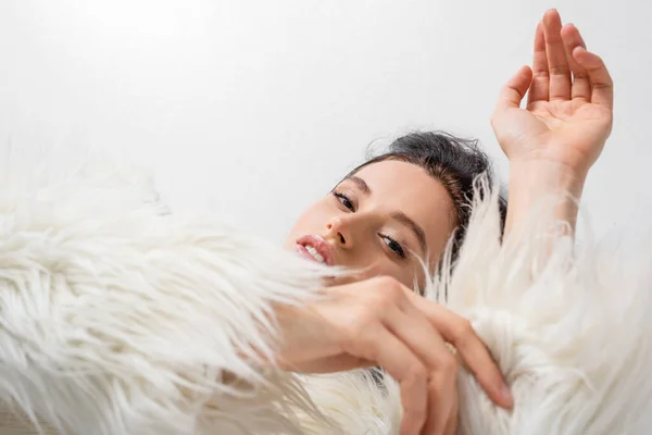 Draufsicht der eleganten brünetten jungen Frau in stilvoller Kunstpelzjacke posiert auf weißem Hintergrund — Stock Photo