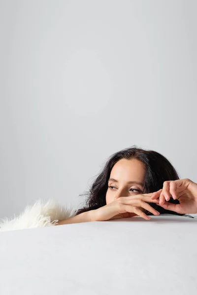 Елегантна брюнетка молода жінка в штучній шубці за кубиком на білому тлі — стокове фото