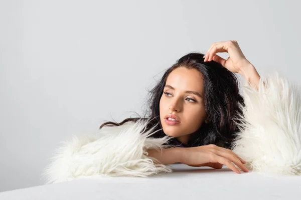 Elegant brunette young woman in faux fur jacket posing near cube on white background — Stock Photo