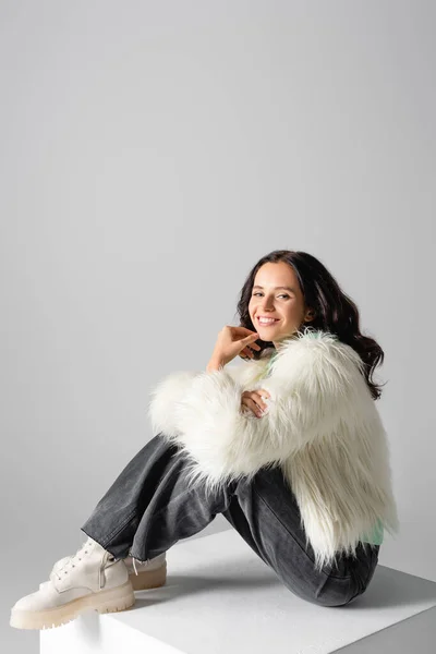 Sonriente morena joven en chaqueta de piel sintética posando sobre fondo blanco - foto de stock