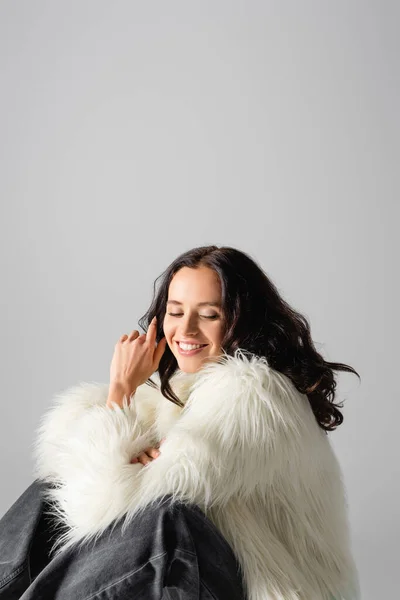 Sonriente morena joven en chaqueta de piel sintética posando sobre fondo blanco - foto de stock