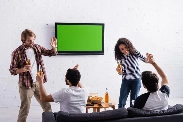 Alegres fãs de esportes multiétnicos dando alta cinco perto lcd tv na parede — Fotografia de Stock