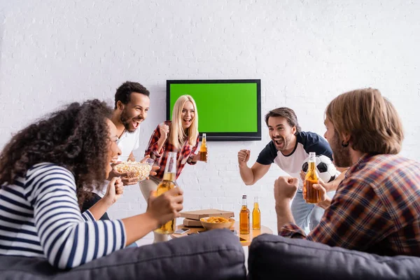 Appassionati di calcio eccitati in possesso di birra e mostrando gesto vincitore vicino tv lcd sulla parete — Foto stock