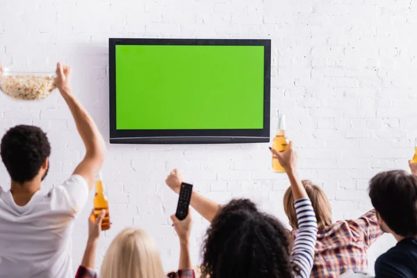 Back view de amigos multiculturais assistindo competição desportiva na tv em primeiro plano borrado — Fotografia de Stock
