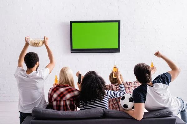 Vista posterior de los fanáticos del fútbol multicultural viendo el campeonato en la televisión y mostrando el gesto ganador - foto de stock