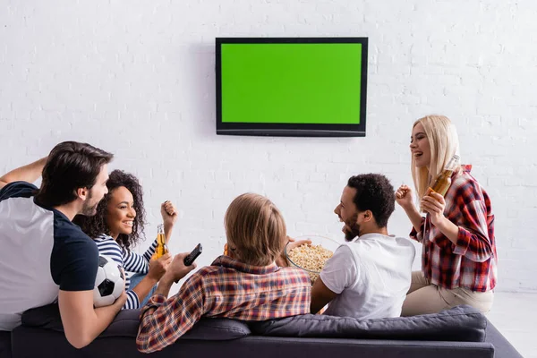 Happy multicultural football fans showing win gesture near led tv on wall — Stock Photo