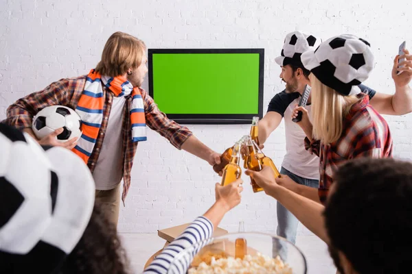 Multikulti-Fußballfans klirren mit Bierflaschen, während sie die Meisterschaft im verschwommenen Vordergrund verfolgen — Stockfoto