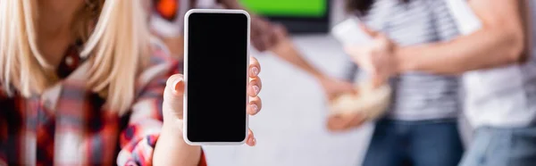 Обрізаний вид жінки, що тримає смартфон з порожнім екраном біля друзів на розмитому фоні, банер — стокове фото