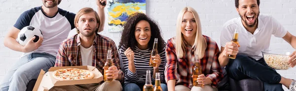 Alegres amigos multiculturales viendo el campeonato de fútbol con cerveza, palomitas de maíz y pizza, pancarta - foto de stock