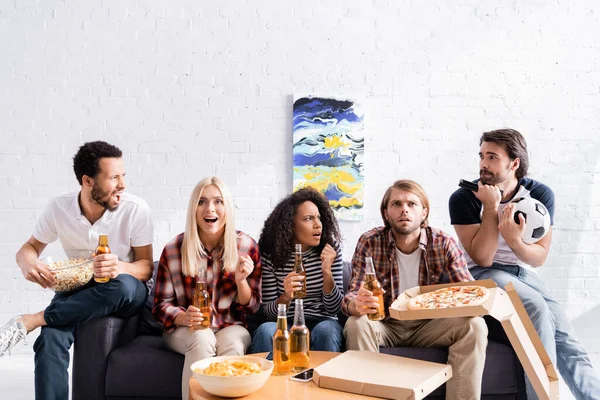 Worried and excited football fans watching championship with beer, pizza and chips at home — Stock Photo