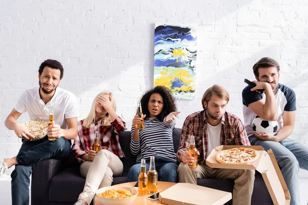 Decepcionada mujer afroamericana apuntando con la mano mientras ve el campeonato de fútbol con amigos multiétnicos molestos - foto de stock