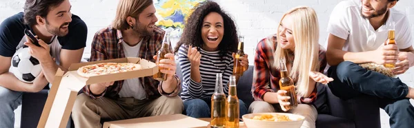 Lachende Afroamerikanerin, die mit dem Finger zeigt, während sie Fußballturniere mit aufgeregten multiethnischen Freunden anschaut, Banner — Stockfoto