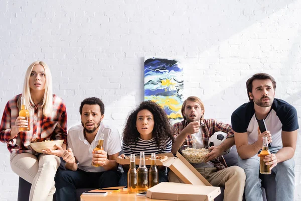 Fãs de futebol multiétnico focados assistindo campeonato com cerveja e lanches em casa — Fotografia de Stock