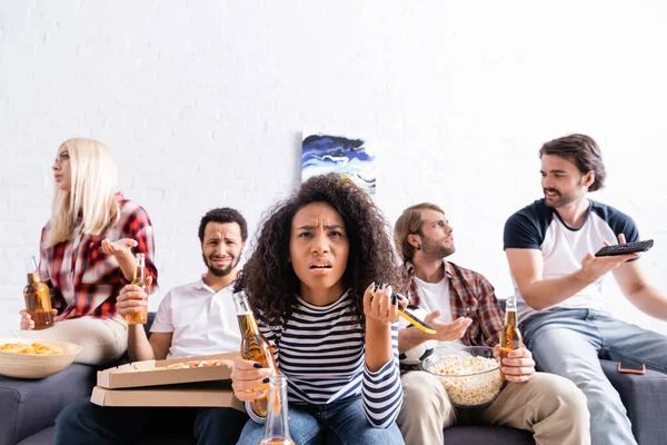 Desapontada afro-americana segurando cerveja e telefone celular perto chateado amigos multiétnicos assistindo campeonato de futebol — Fotografia de Stock