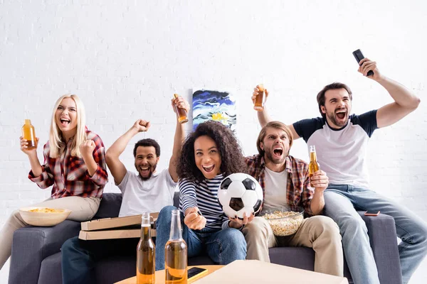 Amigos multiétnicos animado mostrando gesto de vitória enquanto assiste campeonato de futebol em casa — Fotografia de Stock