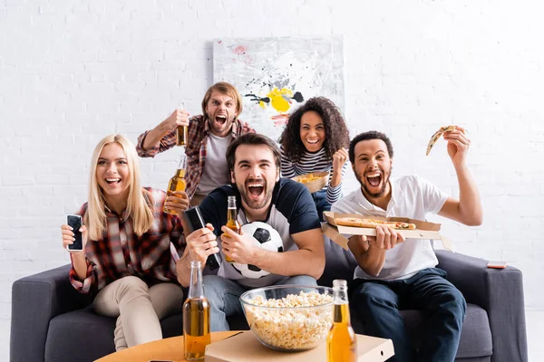 Emocionados fanáticos del fútbol multicultural gritando mientras ven el campeonato en casa - foto de stock