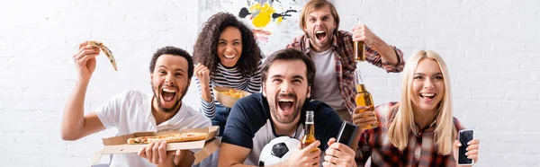 Amigos multiculturales emocionados gritando mientras ven el campeonato de fútbol con pizza y cerveza, pancarta - foto de stock