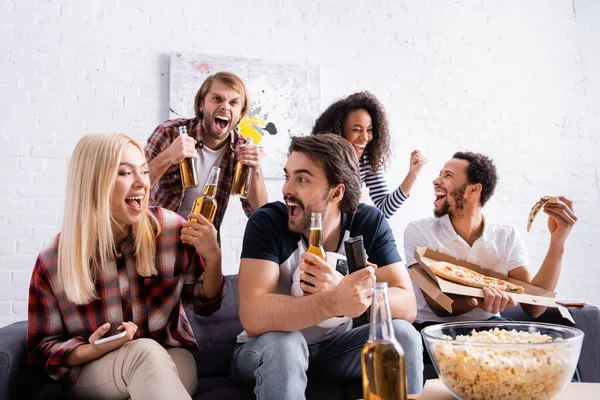 Entusiastas de los deportes sosteniendo botellas de cerveza mientras ven la competencia en casa - foto de stock