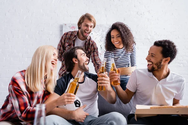 Happy multiethnic football fans holding beer and pizza on blurred foreground — Stock Photo