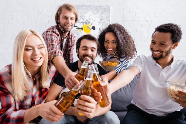 Cheerful multicultural friends clinking bottles of beer on blurred foreground — Stock Photo